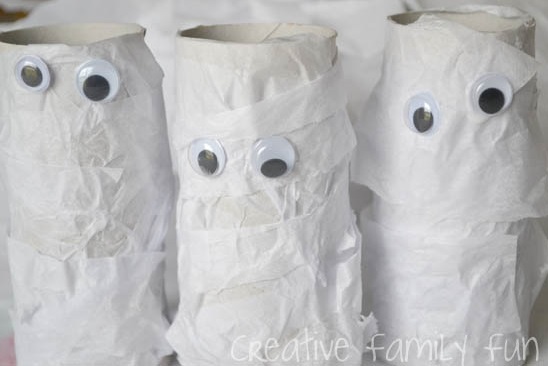 Empty cardboard tube wrap with toilet paper stripes decorated with googly eyes to make mummy for Halloween.